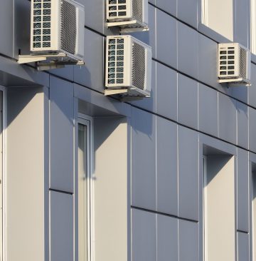 Gray wall of office building made of metal plates with windows and air conditioners